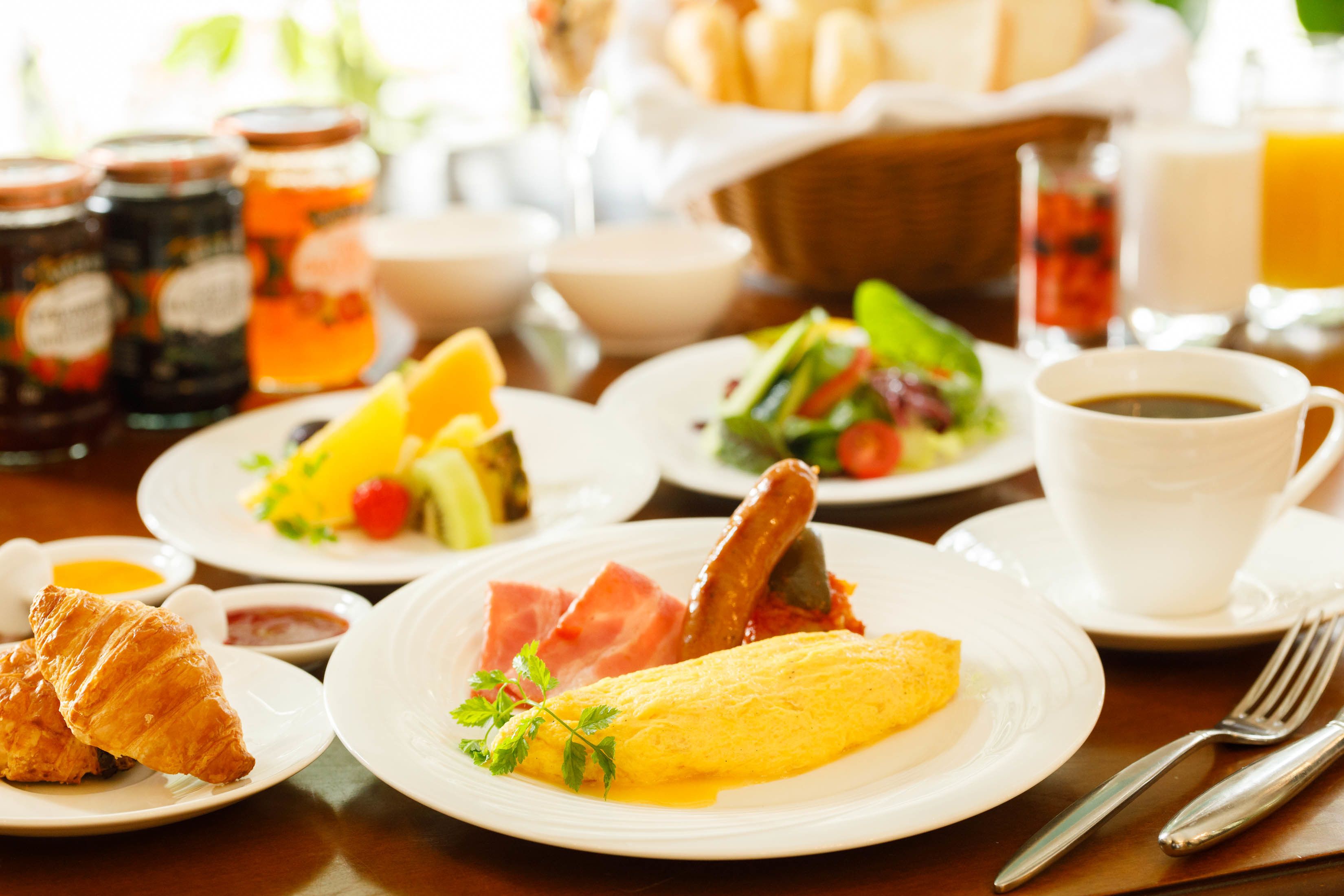 A breakfast setting with plates of food, including croissants, omelets, and a salad.