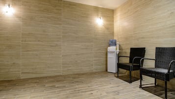A room with a water dispenser, two wicker chairs, and a tiled floor.