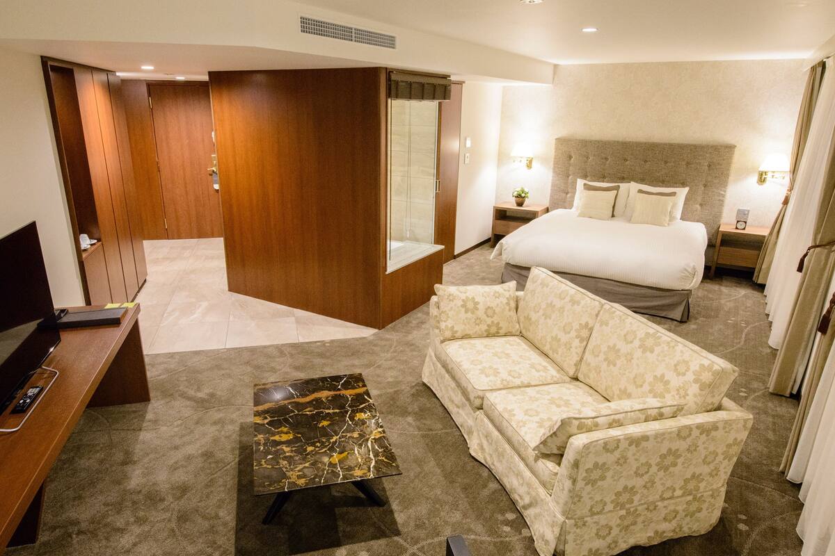 A hotel room with a bed, a sofa, a desk, and a small table.