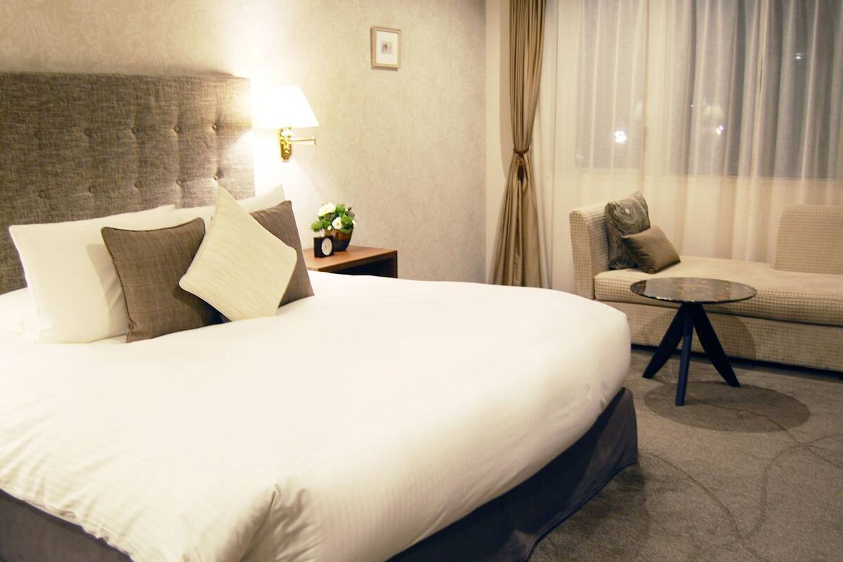 A hotel room with a large bed, a bedside table with a lamp, a small round table, and a sofa.