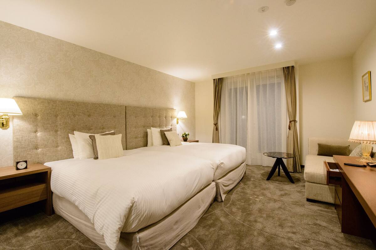 A hotel room with a large bed, two bedside tables with lamps, a small table, and a chair.