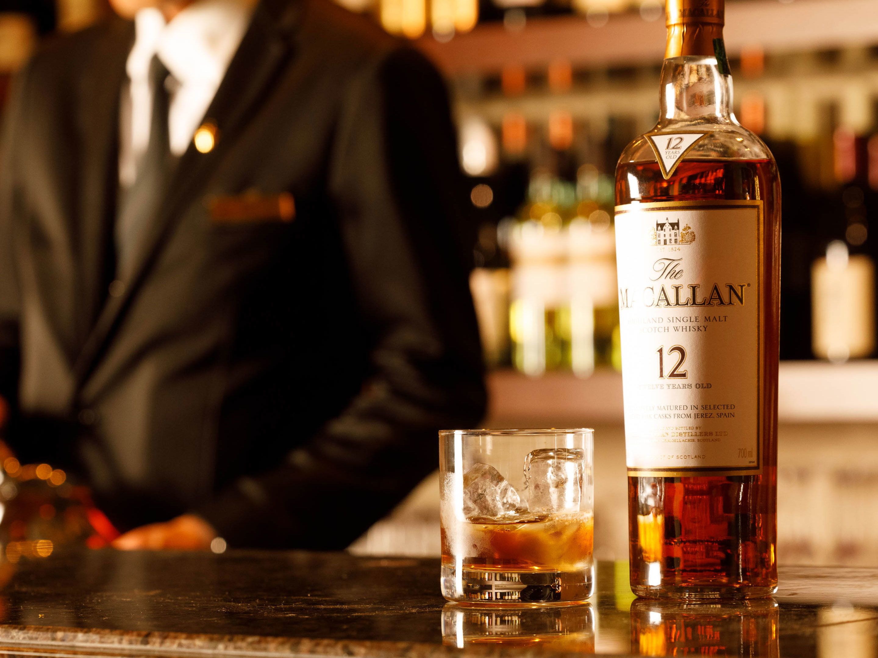 A bottle of The Callan 12 Scotch whisky on a bar counter with a glass of whisky.