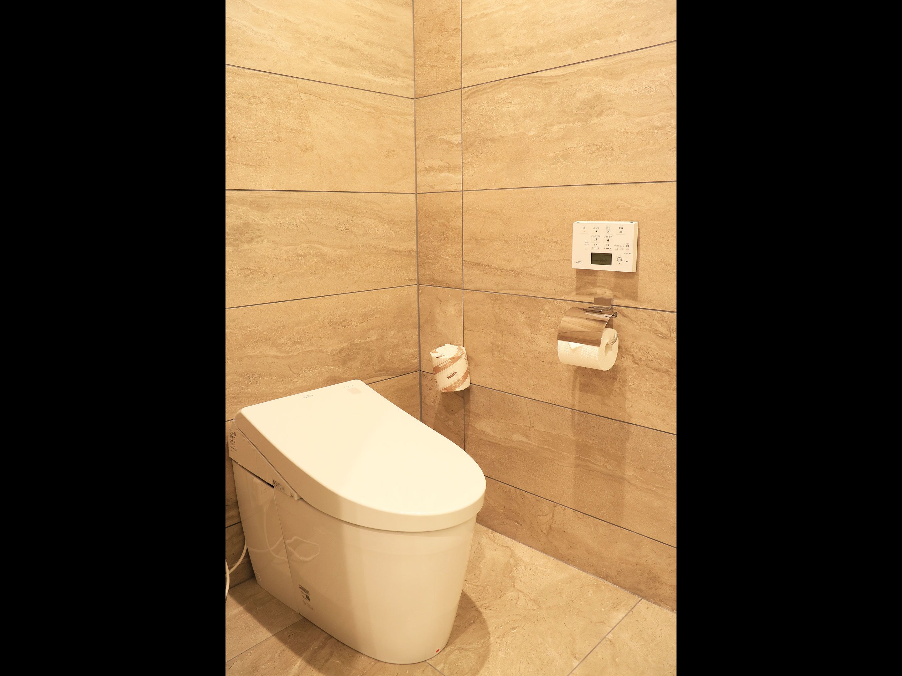 A modern bathroom with a toilet, a hand dryer, and a paper towel dispenser on the wall.