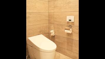 A modern bathroom with a toilet, a hand dryer, and a paper towel dispenser on the wall.