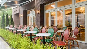 An outdoor seating area with wicker chairs and tables, a brick building, and a glass door entrance.