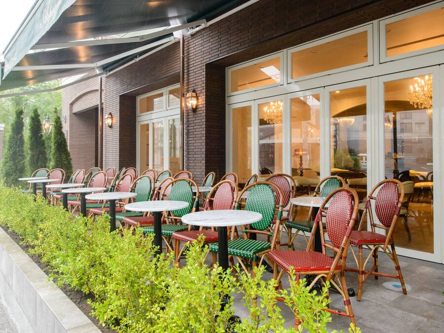 An outdoor seating area with wicker chairs and tables, a brick building, and a glass door entrance.
