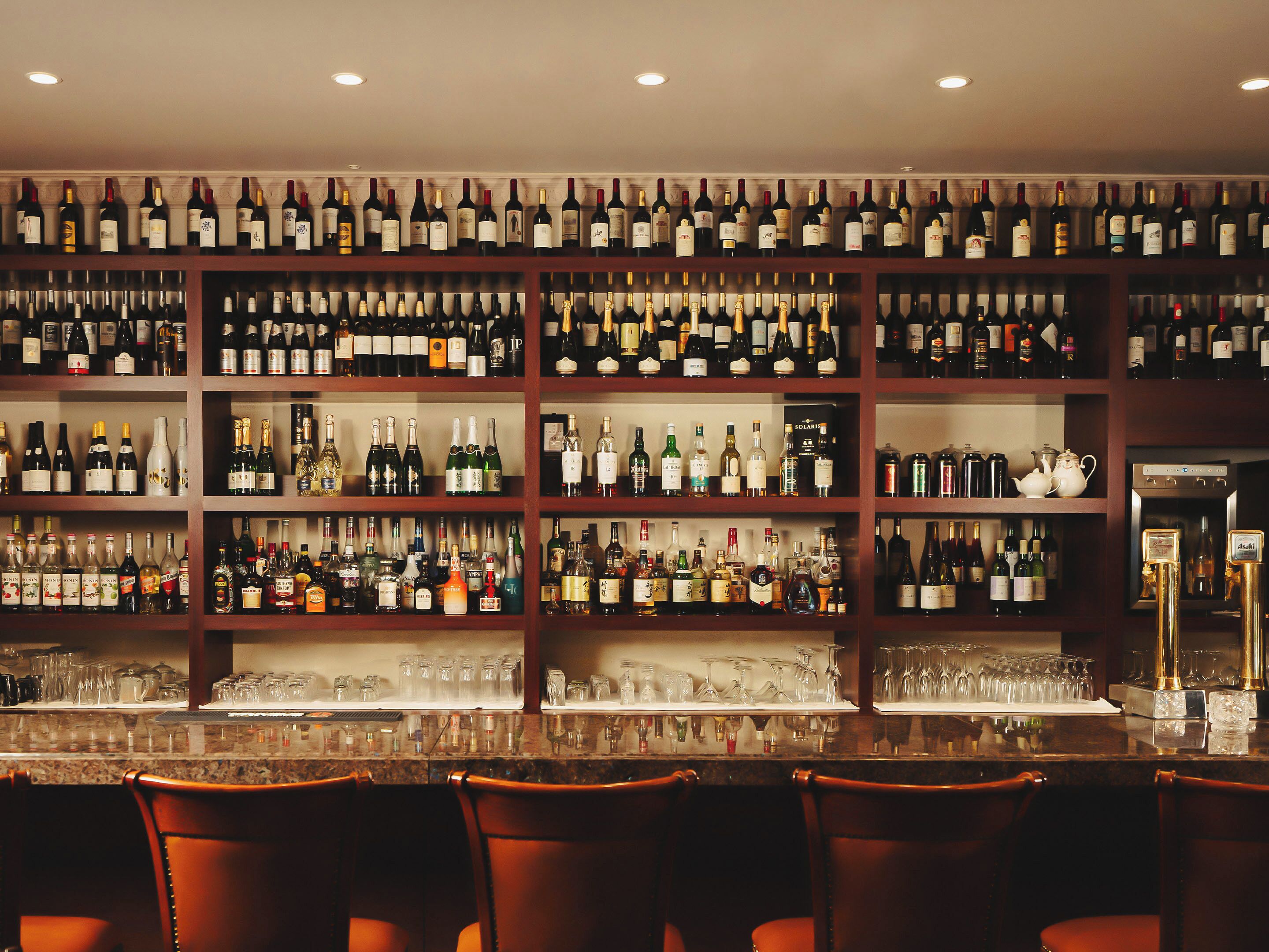 Una zona de bar con varias estanterías llenas de botellas de vino y copas.