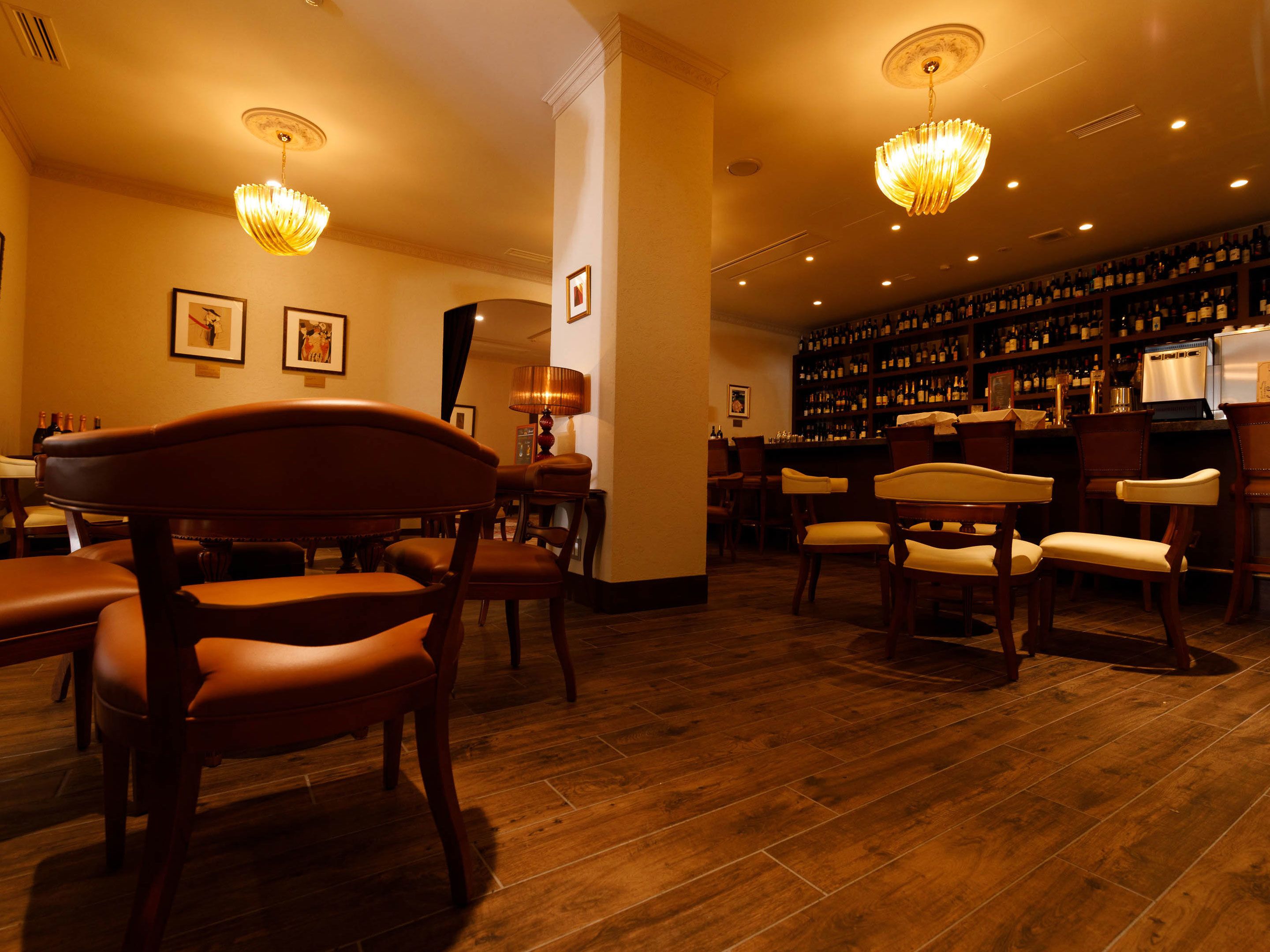 A bar area with wooden flooring, bar stools, and a wall of liquor bottles.