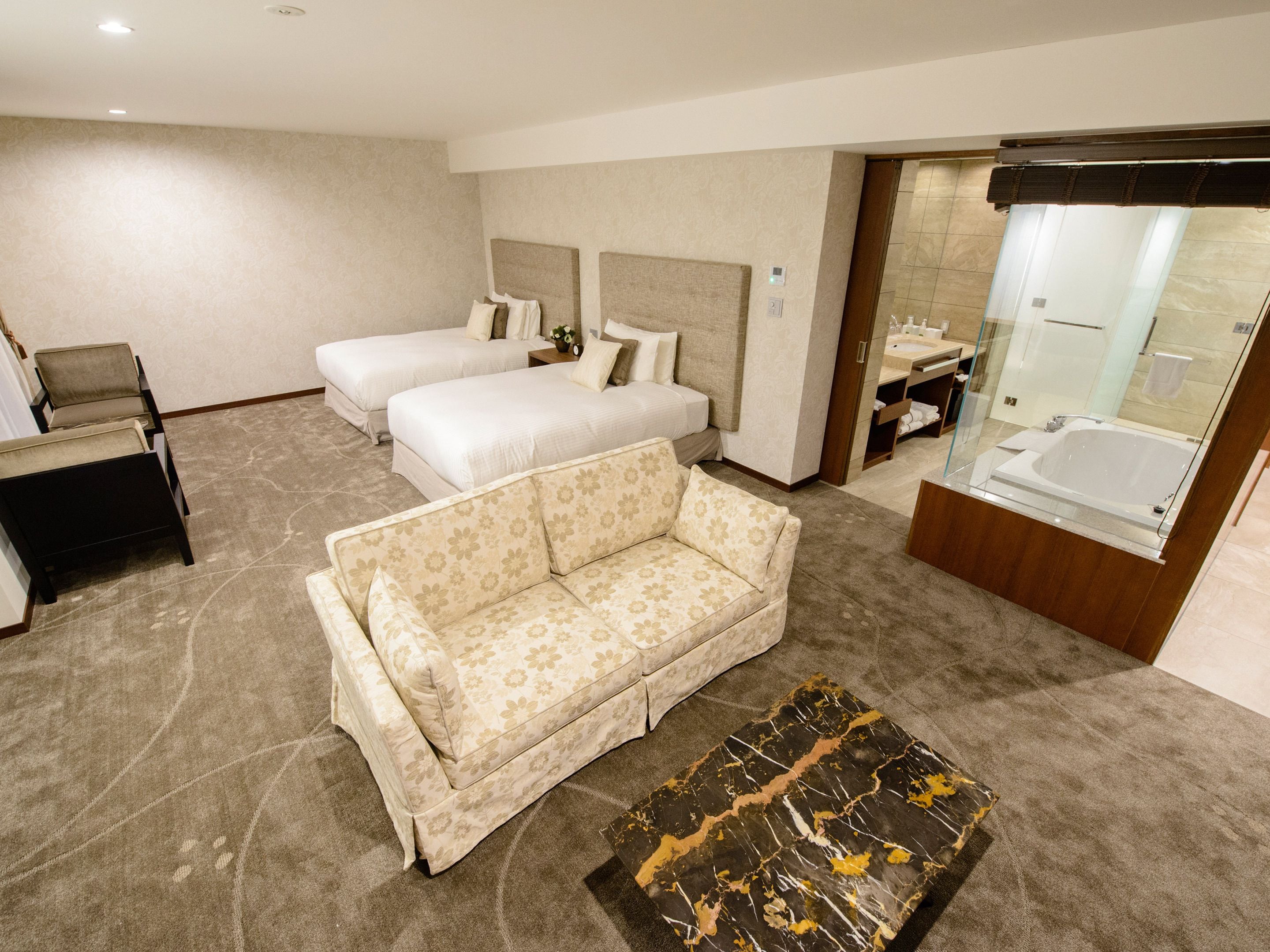 Quarto de hotel com duas camas, um sofá, uma mesinha e banheiro com banheira.