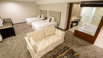Quarto de hotel com duas camas, um sofá, uma mesinha e banheiro com banheira.