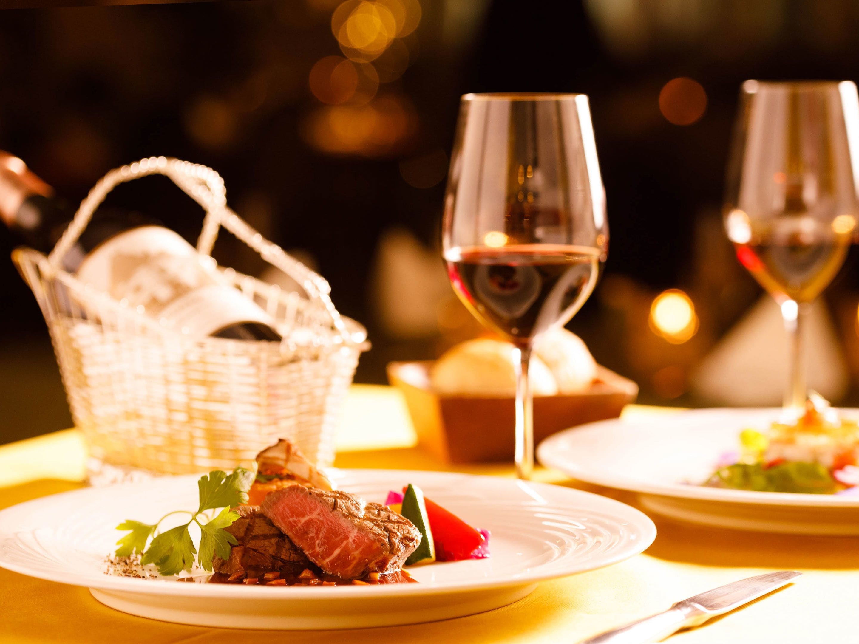 Una mesa de comedor con platos de comida, copas de vino y una cesta.
