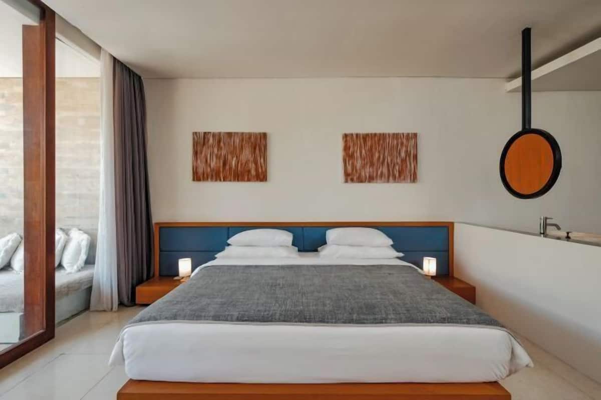 A modern bedroom with a large bed, bedside tables, a hanging mirror, and a view of the outside.