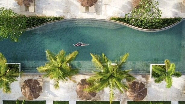 An aerial view of a swimming pool surrounded by palm trees and greenery. - Origin Lombok (Kuta)