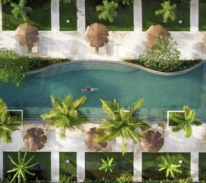 An aerial view of a swimming pool surrounded by palm trees and greenery. - Origin Lombok (Kuta)