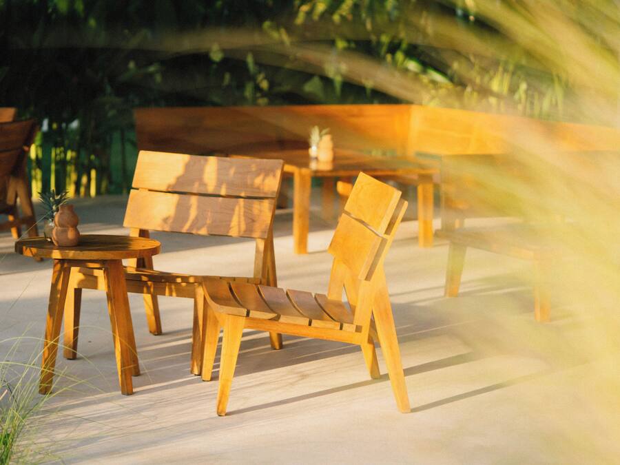 A wooden outdoor seating area with a round table and chairs, surrounded by greenery.