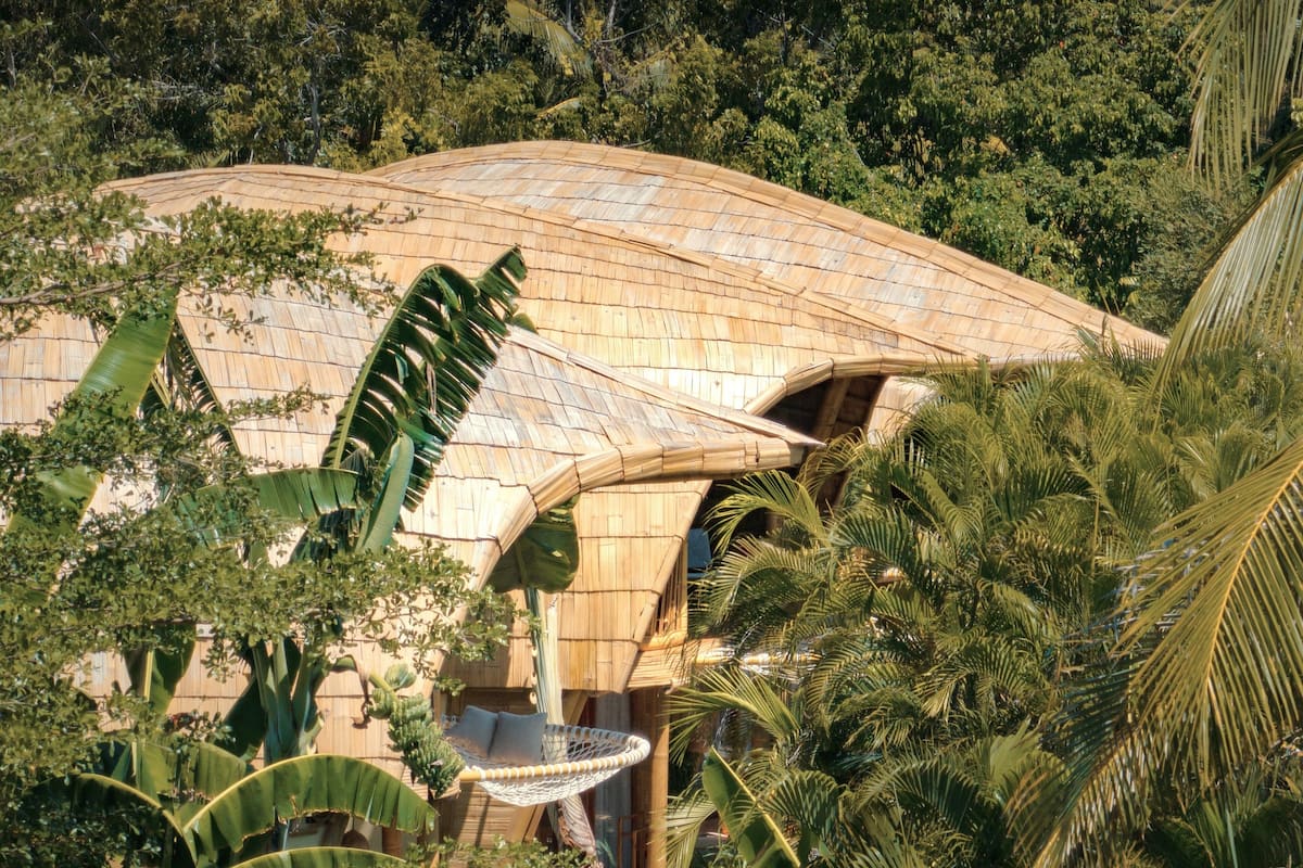 A large, curved building with a thatched roof, surrounded by lush tropical vegetation.