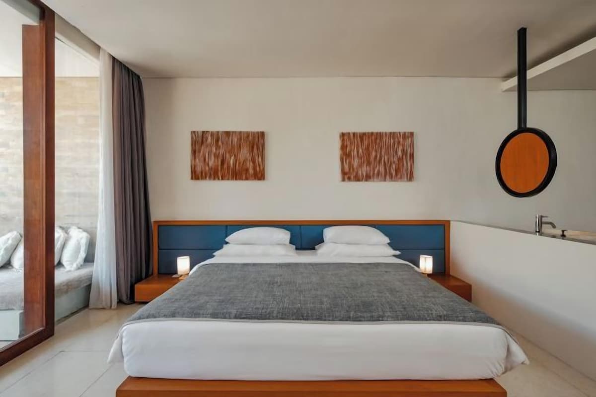 Een moderne slaapkamer met een groot bed, nachtkastjes, een hangspiegel en uitzicht op het omliggende landschap.