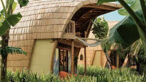 A thatched-roof building with a balcony, surrounded by lush greenery. - Origin Lombok (Kuta)