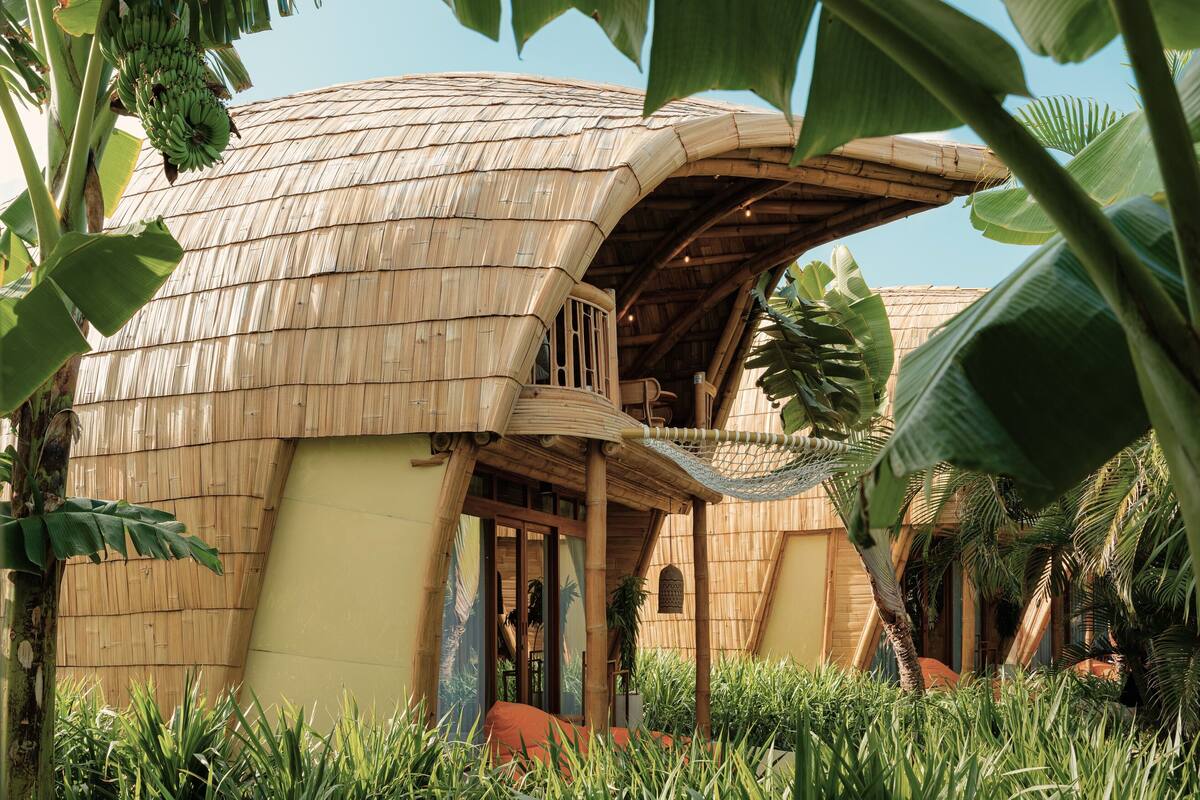 A thatched-roof building with a balcony, surrounded by lush greenery.
