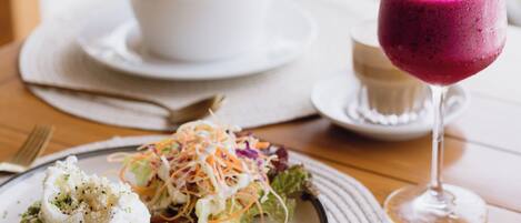 A table with a plate of food, a glass of smoothie, and a bowl of salad.