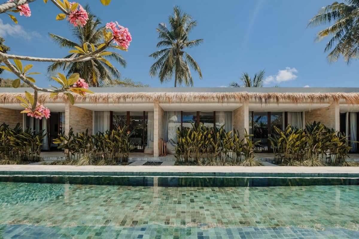 A resort with a pool, thatched-roof buildings, and tropical plants.