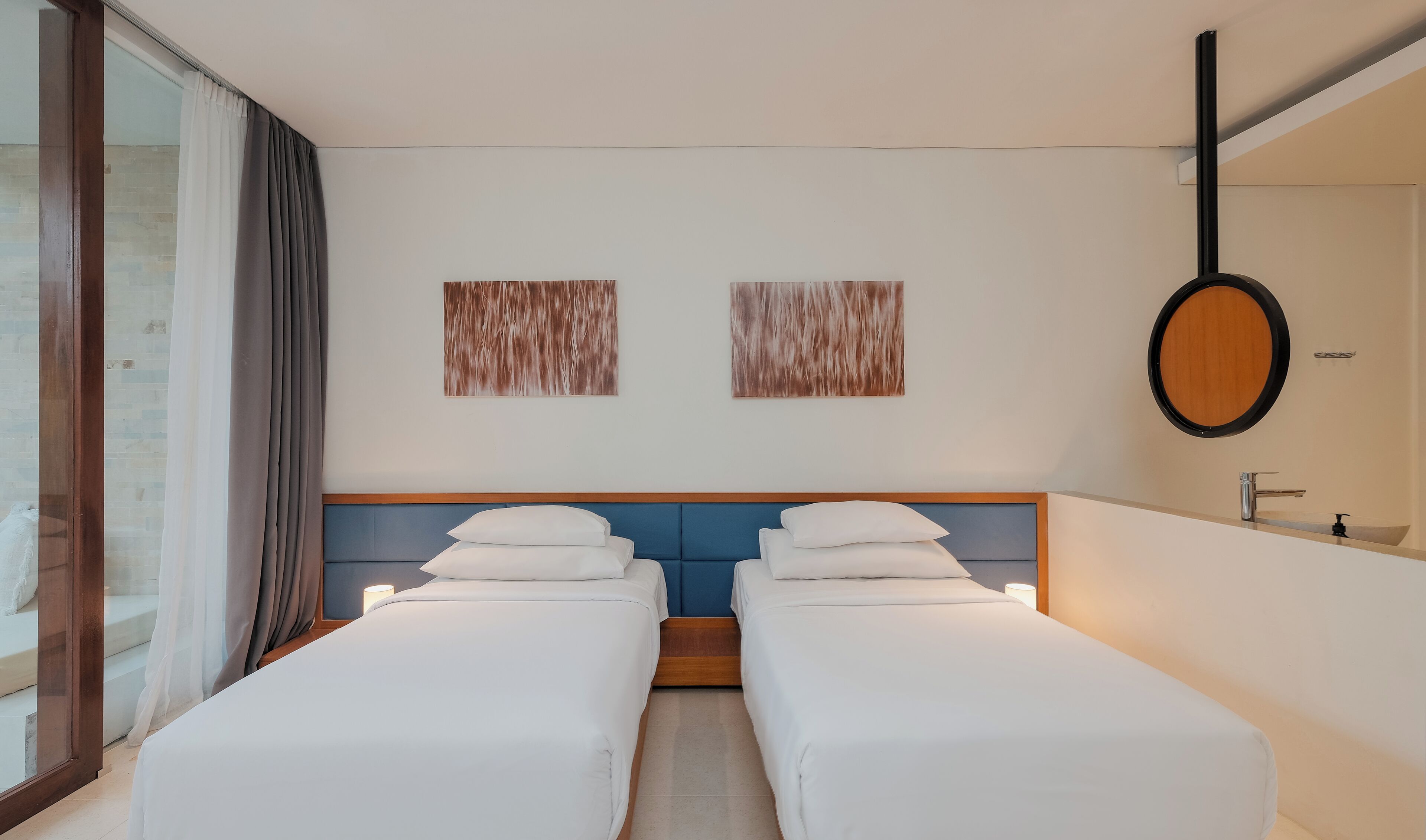 Une chambre d’hôtel avec deux lits simples, un grand miroir et deux œuvres d’art abstraites accrochées au mur.