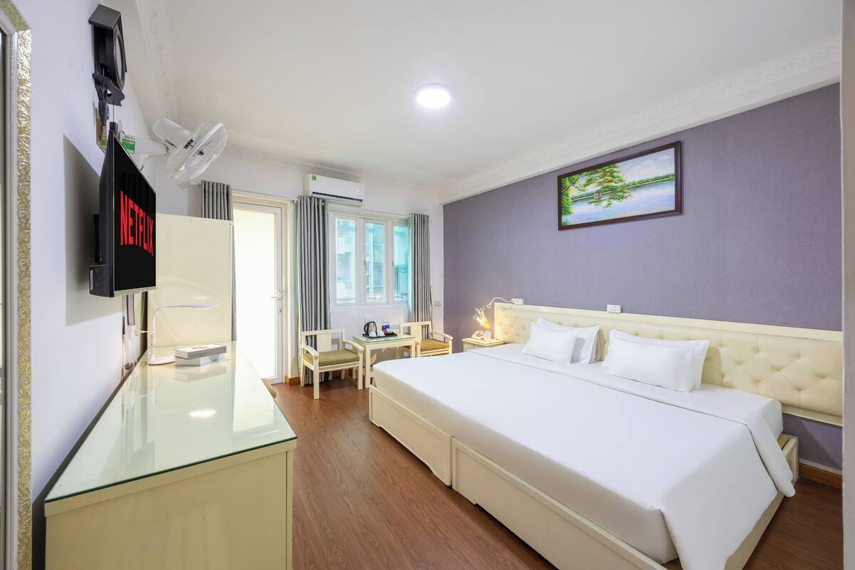 Une chambre d’hôtel équipée d’un lit, d’une table de chevet, d’un bureau, d’une chaise, d’une télévision et d’une fenêtre avec des rideaux.