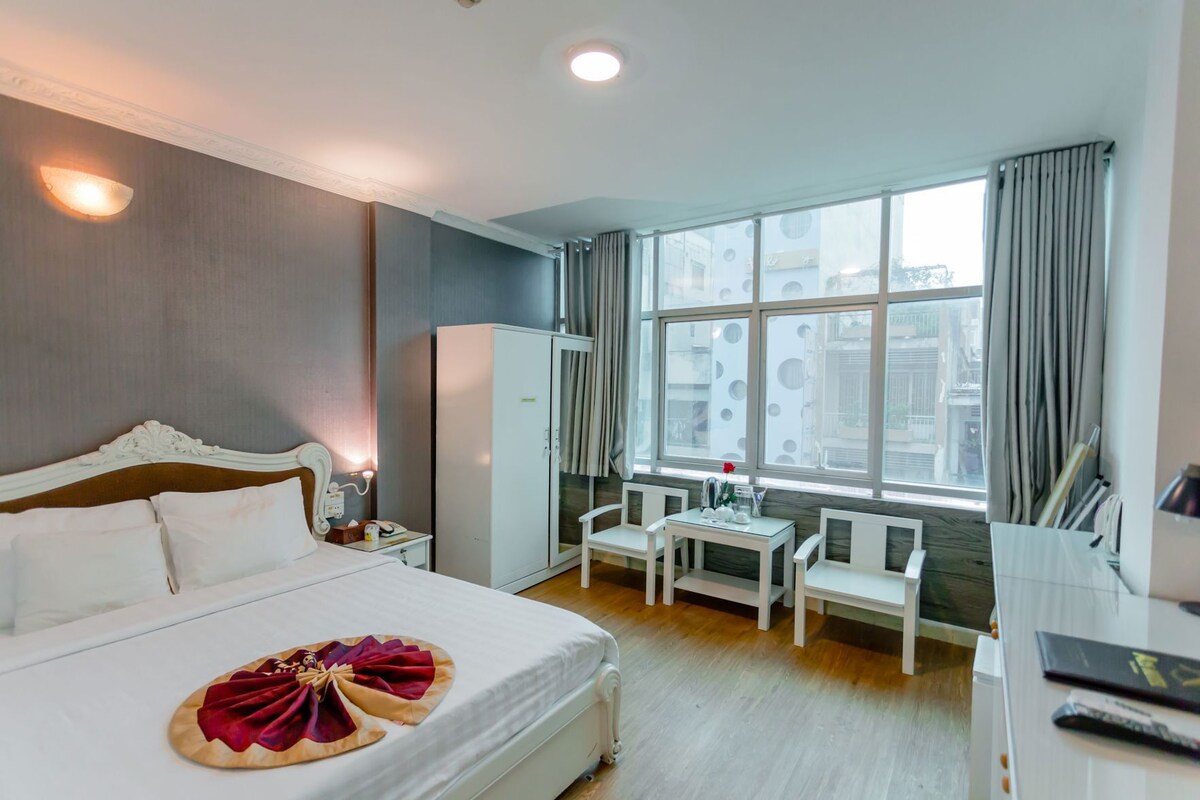 A hotel room with a bed, a desk, a chair, a wardrobe, and a window with curtains.