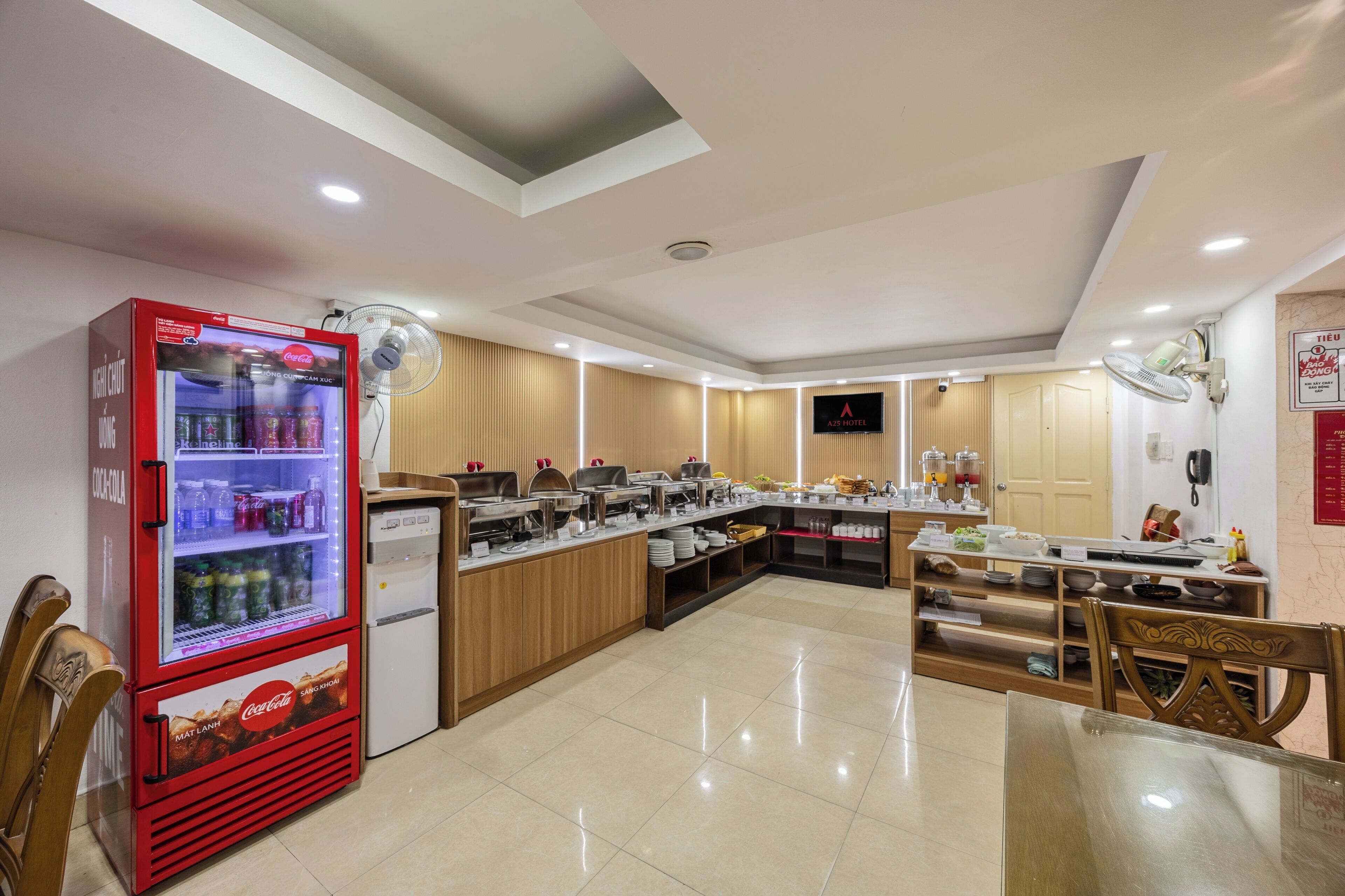 Una cocina de hotel con un refrigerador Coca-Cola, una disposición tipo bufé y armarios de madera.