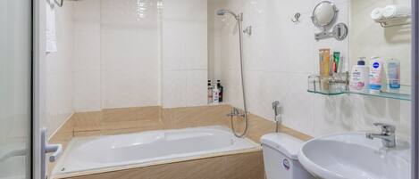 A bathroom with a bathtub, toilet, and sink, featuring a mirror, shelves with toiletries, and a tiled floor.