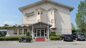 A hotel with a classic facade, a prominent entrance with a red carpet, and a motorcycle parked in front. - Strandhotel Faak (Finkenstein am Faaker See)