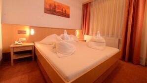 A hotel room with a large bed, two bedside tables, a nightstand, a painting on the wall, and a window with curtains. - Strandhotel Faak (Finkenstein am Faaker See)