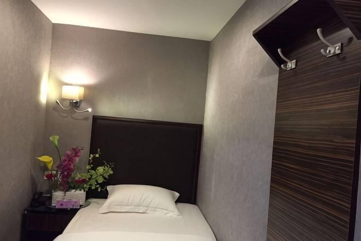 A hotel room with a bed, a nightstand with a lamp, and a wall-mounted shelf.