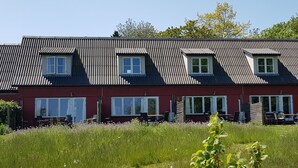 A row of red-roofed buildings with multiple windows and outdoor seating areas. - Pyttegaarden Apartments (Gudhjem)