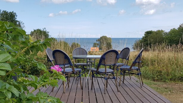 A deck with a table and chairs overlooking a body of water. - Pyttegaarden Apartments (Gudhjem)