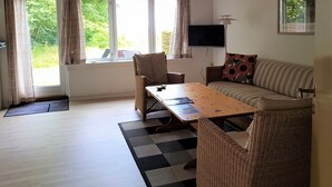 A room with a wooden ceiling, a sofa, a table, and a TV on the wall. - Pyttegaarden Apartments (Gudhjem)