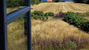 A view from a window overlooking a grassy field with a distant body of water and a small building. - Pyttegaarden Apartments (Gudhjem)