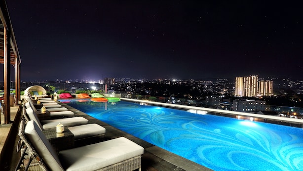 A rooftop infinity pool with lounge chairs and a view of the city at night. - Belviu Hotel Bandung (Bandung)