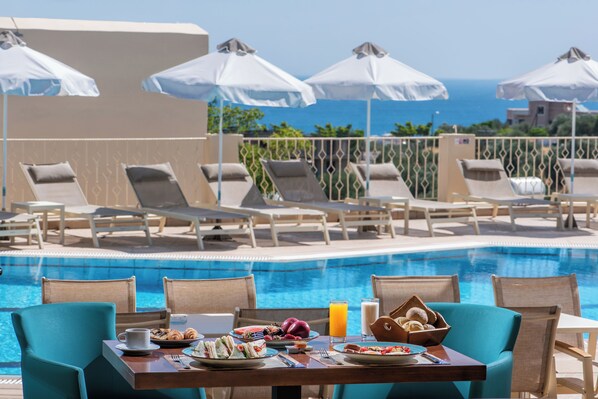 A poolside dining area with lounge chairs, umbrellas, and a table set with breakfast. - Lofos Apartments (Hersonissos)