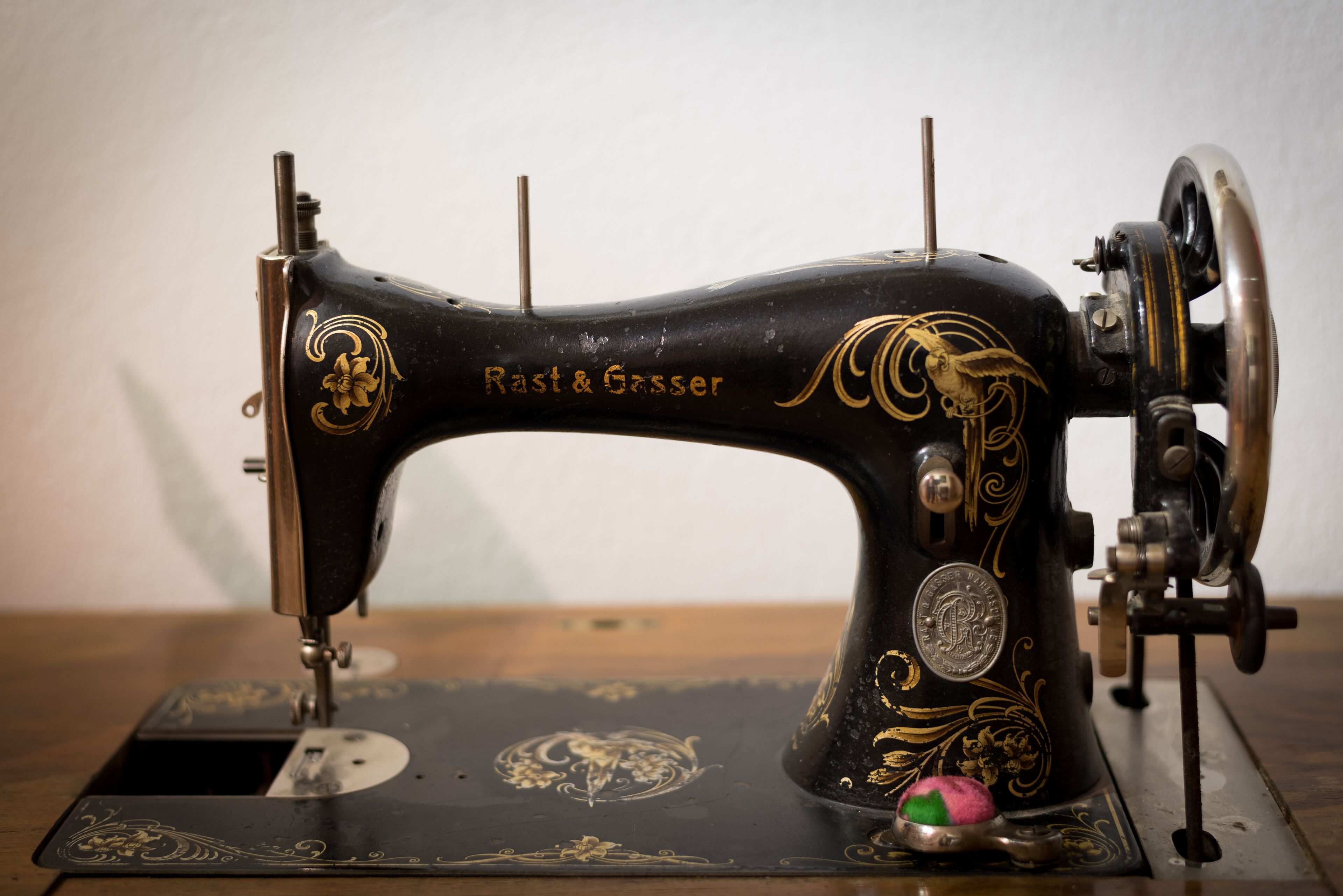 Una máquina de coser antigua con detalles dorados ornamentales y el nombre de la marca “Rast & Gesser” visible en el cuerpo.