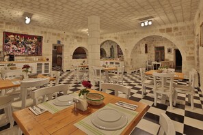 A restaurant with checkered flooring, white chairs, and tables set for dining. - Jacob's Cave Suites (Avanos)