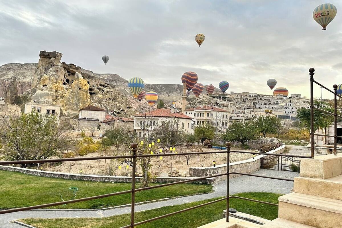 Un pueblo histórico con formaciones rocosas singulares y coloridos globos aerostáticos al fondo.