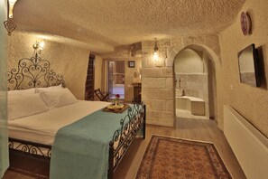 A bedroom with a bed, a nightstand, a mirror, and a stone wall. - Jacob's Cave Suites (Avanos)
