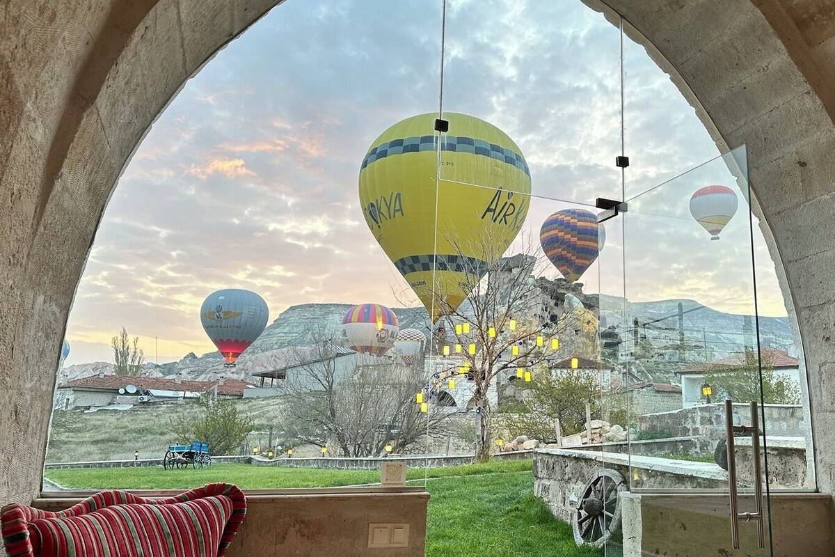 Vista a través de un ventanal arqueado de una habitación con un gran ventanal que da a un paisaje con globos aerostáticos.