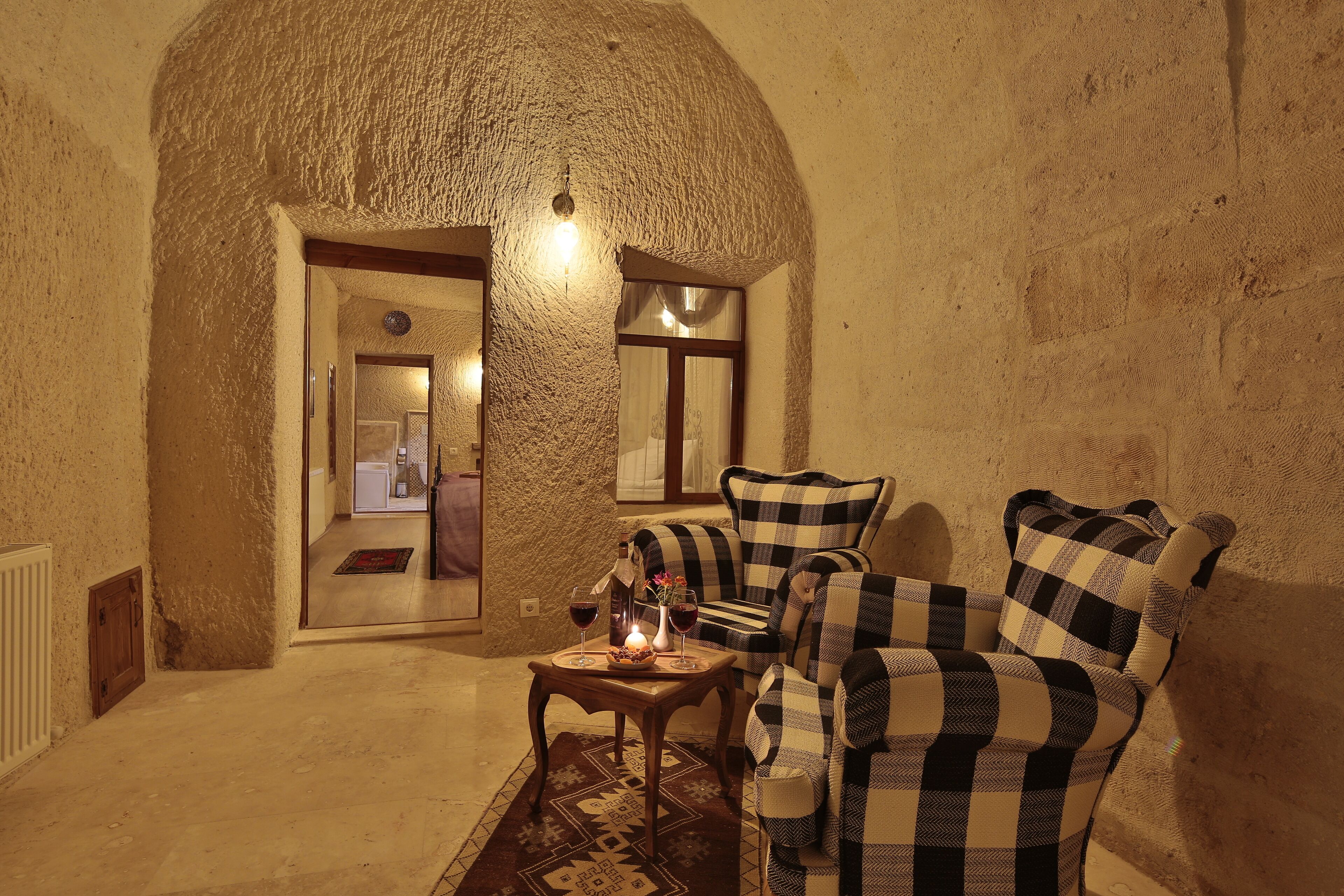 A cozy room with a checkered sofa, a small table with a candle, and a rustic stone wall.