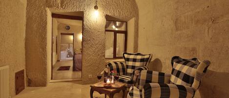 A cozy room with a checkered sofa, a small table with a candle, and a rustic stone wall.