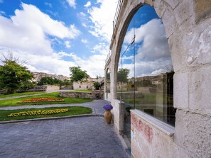 A courtyard with a paved walkway, a stone wall, and a glass window reflecting the sky. - Jacob's Cave Suites (Avanos)