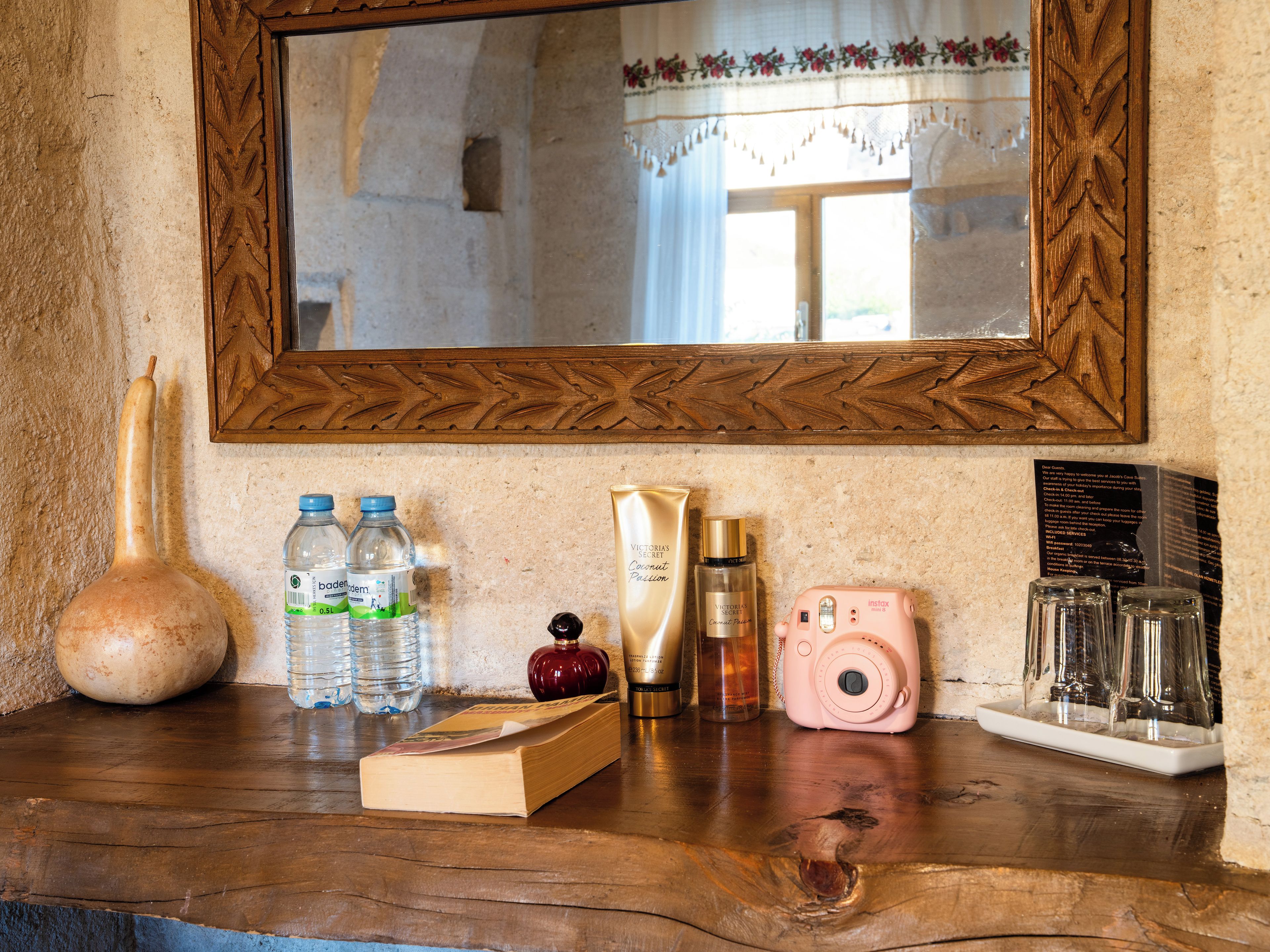 Un tavolo in legno con uno specchio, un vaso, bottiglie d'acqua, un libro, un flacone di profumo, una macchina fotografica e occhiali.