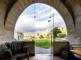 Una habitación con un sofá estampado, una mesa y un vidrio que da a un espacio exterior con vistas a una colina y edificios.