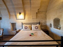Un dormitorio con una cama, una mesita de noche, una lámpara de pared y una pared de piedra.